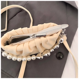 Détail du mini sac plissé beige avec chaîne en perles et cœurs sur un blazer gris