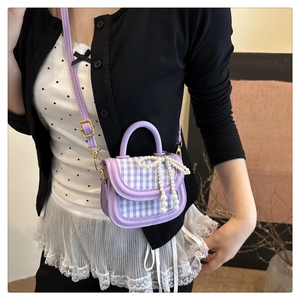 Detail of a purple plaid mini handbag featuring a pearl bow charm and adjustable strap