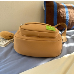 Détail du sac bandoulière en toile marron avec étiquette M verte et fermeture éclair
