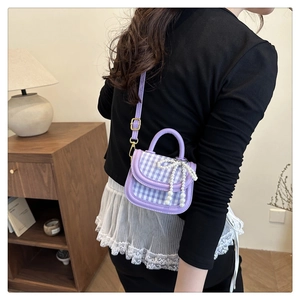 Detail of purple plaid mini crossbody bag featuring a pearl bow and gold clasp