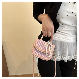 Detail of mini pink plaid handbag with pearl bow decoration worn over the shoulder