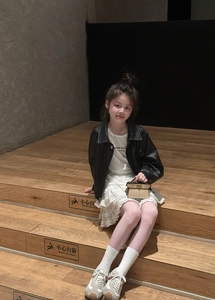 Girl wearing black leather jacket and white lace skirt holding a mini top handle chain bag