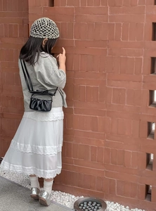 Toddler girl wearing gray knit top with layered white lace skirt and black pleated handbag