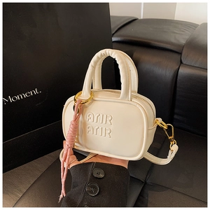 Détail du mini sac bandoulière crème avec lettres embossées et pendentif rose