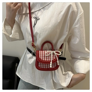 Detail of red gingham mini bag featuring pearl bow charm and elegant crossbody strap