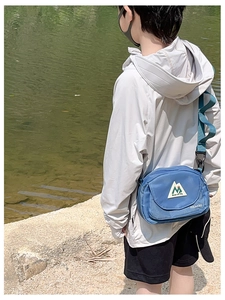 Detailed outdoor view of a kid's blue nylon crossbody bag featuring green mountain logo