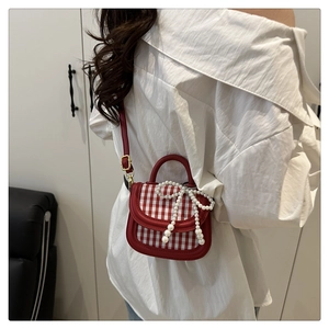 Close-up of mini red plaid bag with pearl bow detail and adjustable shoulder strap