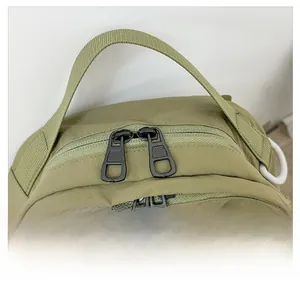 Macro detail of olive green nylon backpack featuring smooth dual black metal zippers and handles