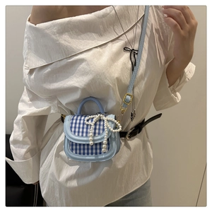 Detail of blue plaid mini bag with pearl bow charm worn by a model in white shirt