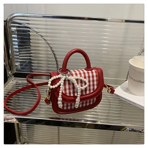 Detailed view of red plaid handbag featuring pearl bow ornament on stripe tray