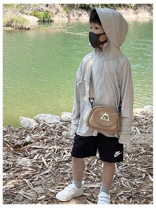Outdoor close-up of a child wearing a brown crossbody bag and grey sun protection jacket