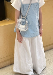 Détail d'un sac à main argenté en forme de lune avec un nœud en dentelle sur un jeune mannequin