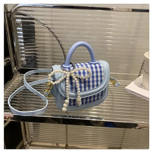 Close-up of light blue plaid mini bag with pearl bow charm and golden metal buckle