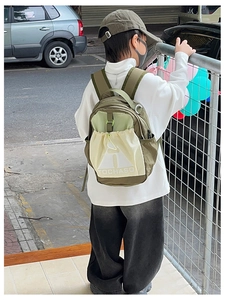 Rear view of a child wearing a green and beige contrast backpack in a city street setting