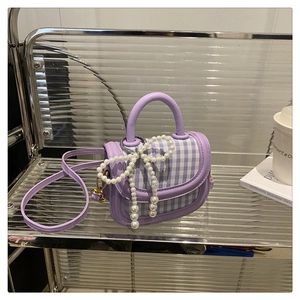 Detail of purple plaid mini bag featuring a large pearl bow charm and leather strap