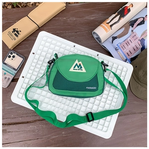 Outdoor lifestyle shot of a green canvas crossbody bag with logo on a white tray