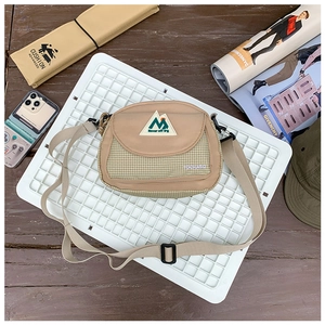 Flat lay of khaki canvas crossbody bag with mountain patch on white grid tray