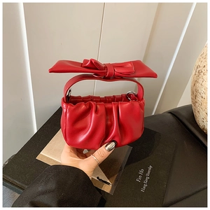 Detail of red cloud bag featuring a large bow handle and elegant pleated leather design
