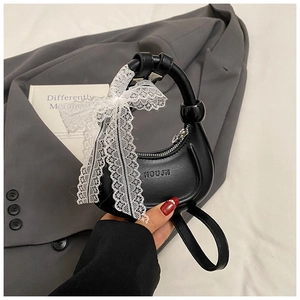 Détail d'un sac à main noir en forme de croissant avec un nœud en dentelle blanche