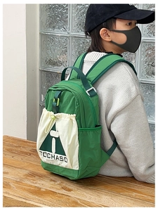 Detailed side view of green kids backpack with white canvas drawstring pocket and straps