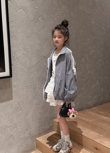 Dettaglio della giacca a quadri blu da bambina con gonna in pizzo bianco e maglietta casual
