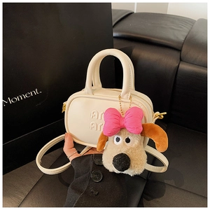 Dettaglio della mini borsa crema con ciondolo a forma di cucciolo e logo goffrato