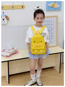 Close-up of yellow canvas kids backpack with a transparent pocket and cute plush ducks