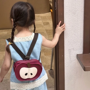 Detail of red apple-shaped mini toddler backpack with adjustable straps on a child