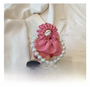 Detail of pink pleated bucket bag with large pearl handle and golden chain strap