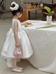 Pink bow handbag and white dress shown on a child model in a minimalist setting
