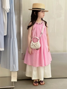 Detail view of a white semi-circular kids crossbody bag with a bow and summer dress outfit