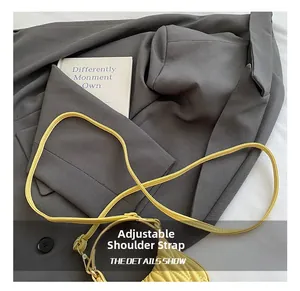 Detail of yellow pleated girls shoulder bag with adjustable strap on a grey fabric background