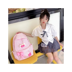 Detail view of pink plaid kids backpack with plush bow decoration in a cozy indoor setting