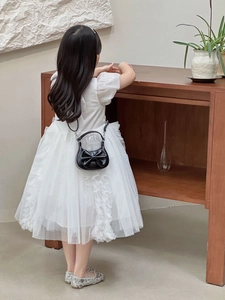 Rear view of child wearing white tulle layered dress with black bow mini handbag