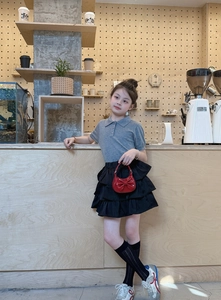 Detail of a red bow handbag paired with a grey knit polo and layered black tutu skirt