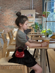 Close-up of a glossy red mini handbag with a bow detail styled with a kids' outfit