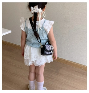 Detail einer Mini-Mädchen-Umhängetasche mit Karomuster, Perlenkette und Schleife am Outfit
