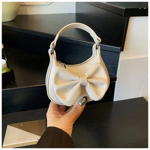 Detail of a creamy white mini handbag featuring a large decorative bow and top handle