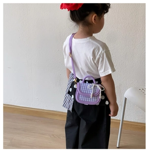 Details einer lila karierten Kinderhandtasche mit Perlschleife und verstellbarem Gurt
