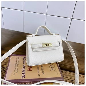 Close-up of white litchi leather mini crossbody bag with gold metal buckle on a book