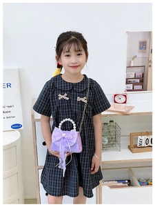 Détail du sac enfant violet avec poignée en perles et nœud en tulle sur une robe à carreaux