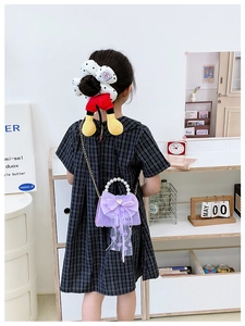 Détail d'un sac fille en dentelle violette avec anse en perles et nœud sur fond bois