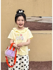 Close-up of kids yellow ruffled t-shirt with ice cream patch and colorful pom-poms