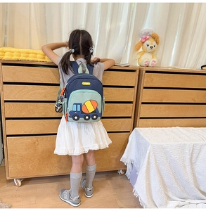Detailed back view of a child wearing the cute cartoon cement mixer backpack in a cozy room