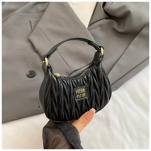 Close-up of black quilted leather girl's mini handbag with gold logo and pleated texture