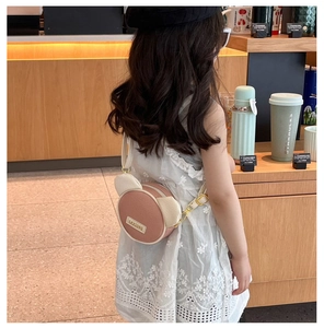 Detail of cute bear-eared round crossbody bag with metal buckle and pink-beige color contrast