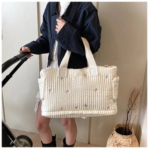 Detail der gesteppten beigen Wickeltasche mit Blumenstickerei und Seitentaschen