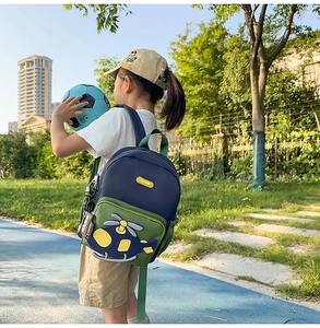 Outdoor view of child wearing blue and green cartoon helicopter backpack in park