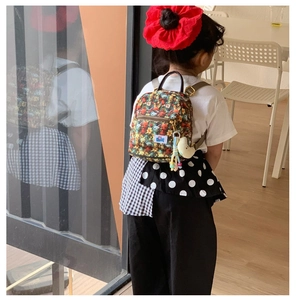 Kid back view wearing a mini floral cartoon backpack with a cute yellow moon plush charm
