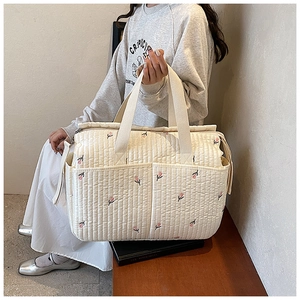 Detailed view of the quilted texture and pink floral embroidery on the beige mommy bag